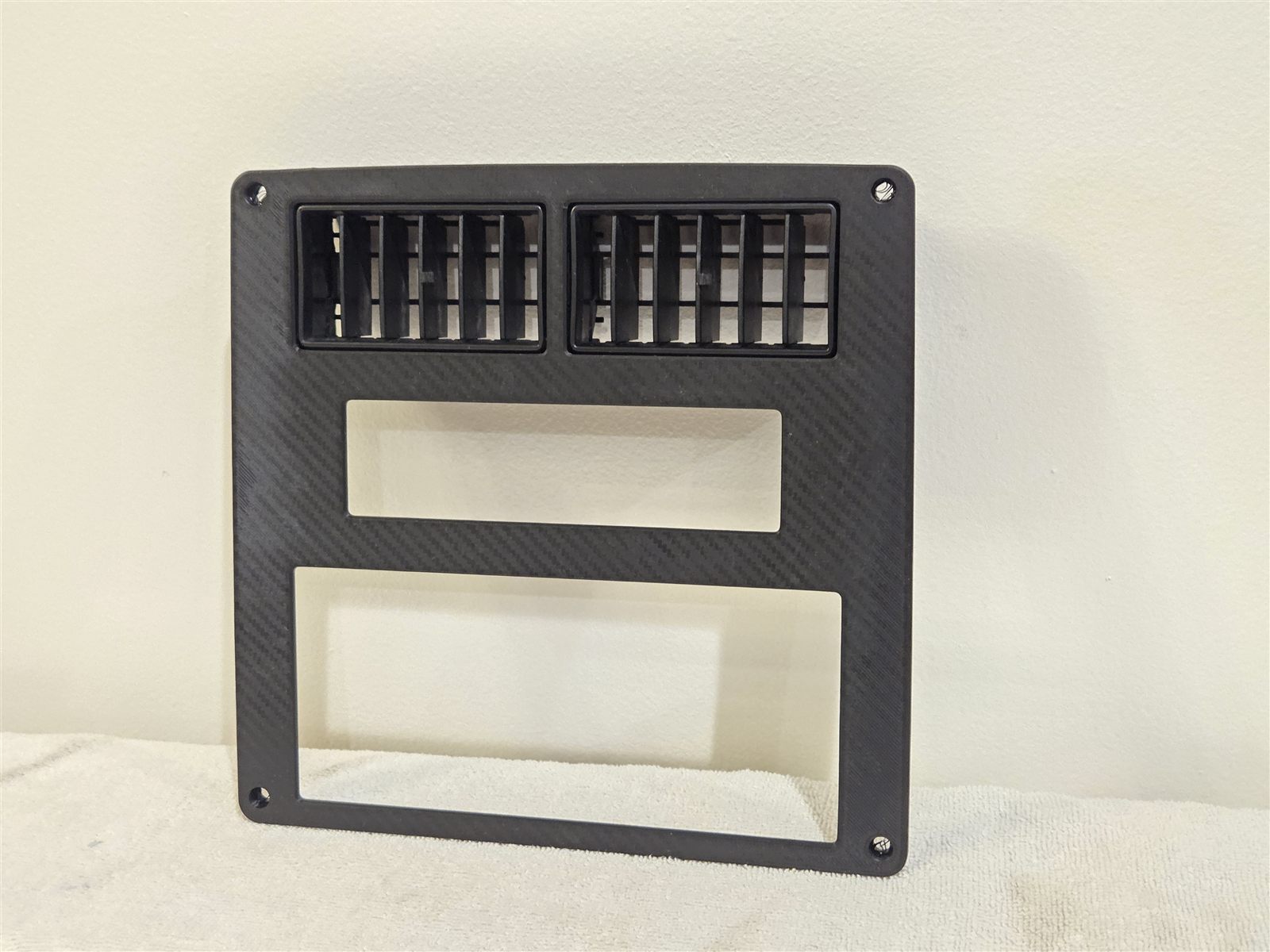 Reproduction Fiero stereo bezel in carbon weave, with the factory air vents clipped in