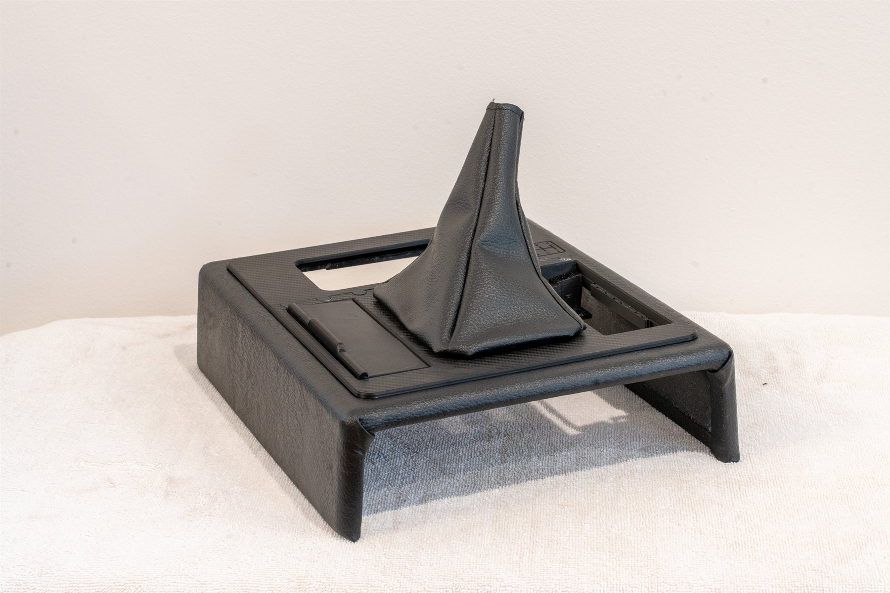 Reproduction Fiero center console frame, upholstered, with a carbon weave shifter bezel, smooth ash tray door and black vinyl shifter boot