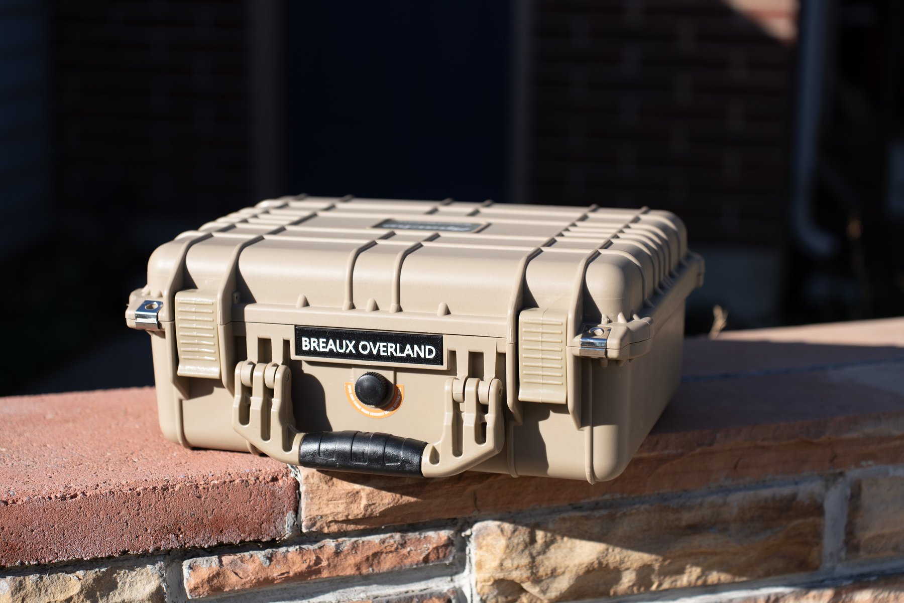 Closed tan Apache 3800 case with a Breaux Overland label on the brick wall