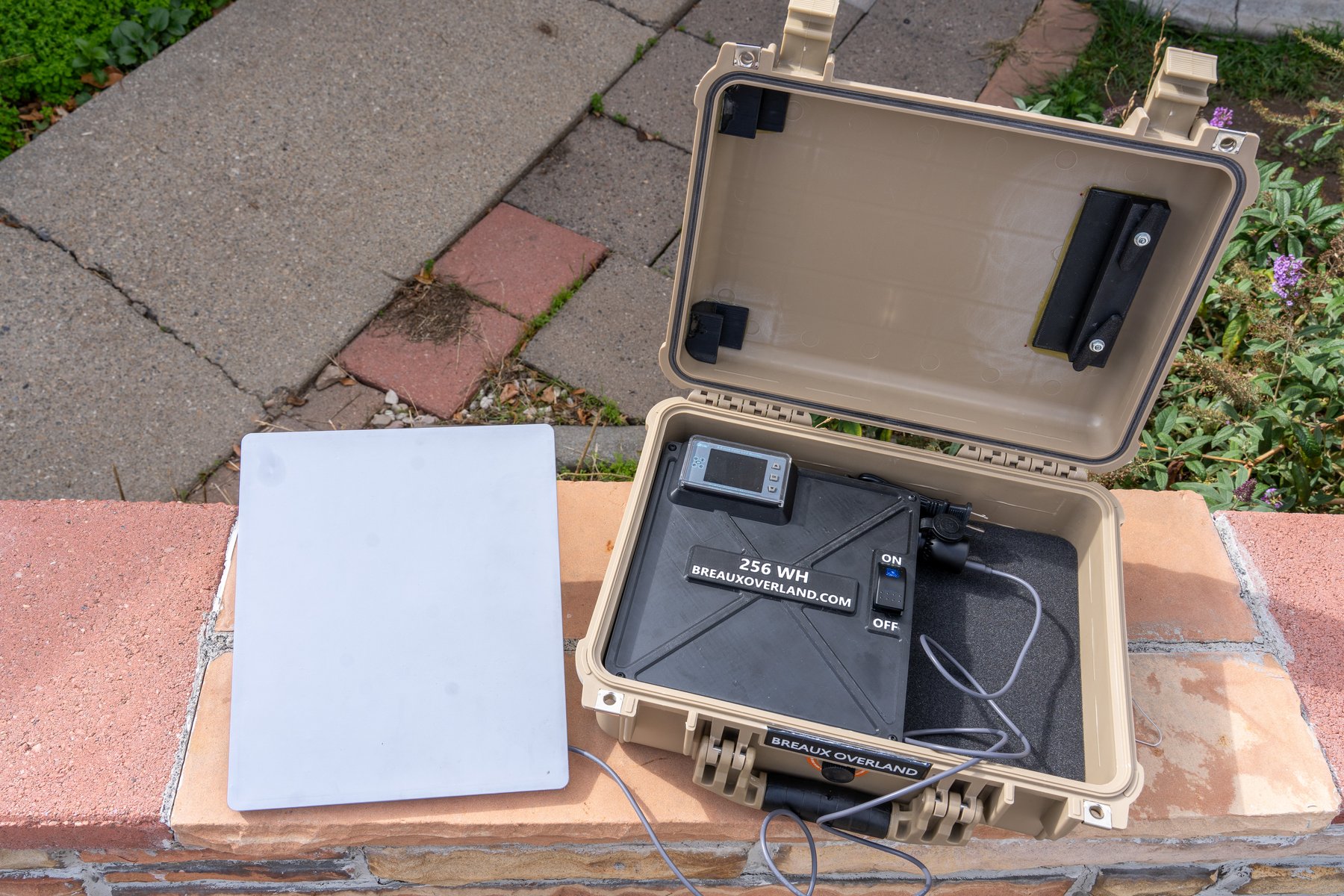 Open Starlink Mini power kit on a brick wall, battery box with meter and lit switch in the case and the dish lying beside it